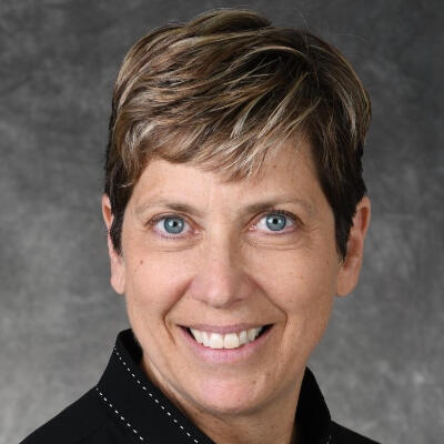White woman with short hair smiling in front of a grey background
